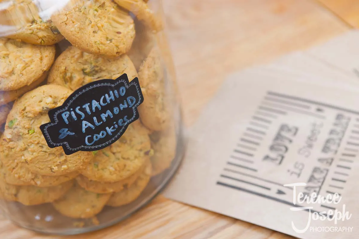 25_County_Arms_Wandsworth_Wedding_Breakfast_Photos A jar filled with pistachio and almond cookies, labeled with a black chalkboard tag, graces the table at a County Arms Wandsworth wedding. Nearby, a paper bag reads, "LOVE is Sweet, take a treat.